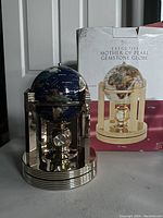 Front view of the gemstone globe on gold-tone stand with clock and original box behind
