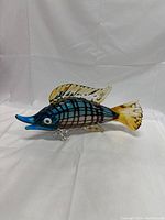 Photo of colorful Murano art glass fish sculpture, side view showing blue and amber-tinted fins and tail, and checkered body pattern.
