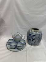 Full view of the blue and white porcelain tea set (teapot, four cups, tray) alongside the decorative vase.