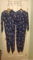 Full front view of two navy blue holiday themed onesies hanging side by side on door