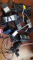Top view photo showing multiple black power adapters and chargers with cables tangled and stacked.