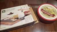 Photo of the wooden cutting board with slate insert set in original box showing cheese utensils to side.