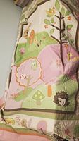 Photo of comforter side with woodland animals and trees in pastel colors on bed.