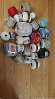 Multiple spools of crochet thread in various colors and brands, mostly new in original packaging, laid out on wooden floor.