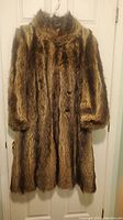 Front view of the long dark brown fur coat hanging on a door, showing the full length and texture of the coat.