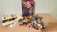 Overall lot showing Ecto-1 vehicle, smaller vehicle, multiple figures, and collectors case