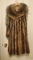 Full view of the fur coat on a hanger, showing the front buttoned body made of multi-tone brown real fur and fur collar.