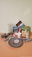 Front view of lot items arranged on table showing drinking glass, ceramic cups, personal care and makeup items