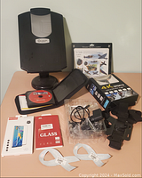 Lot items on orange surface showing black camera parts, mouse pad with WWII planes, glass screen protector box, charger, cables, and ribbon pins.