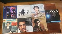 Photo showing seven vinyl LP records featuring Placido Domingo, Paul Anka, Liberace, and other artists arranged on a wooden surface.