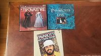 Photo of three vinyl LP albums and one book featuring Luciano Pavarotti on a wooden surface.