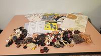 Overview photo of multiple strands of assorted buttons on strings, bags of loose buttons, printed patterns, and various sewing items spread on a table.