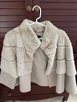 Front view of cream fur cropped jacket hanging on white hanger against wooden backdrop