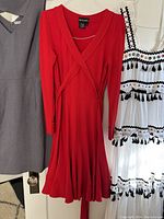 Three ladies dresses hanging on a door, gray short-sleeved dress on left, red long sleeve dress center, white sleeveless dress with tassels on right