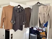 Five ladies' sweaters and cardigans hanging on hangers against a white background.