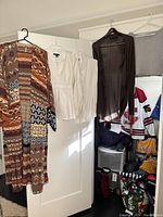 Full view of all five pieces of clothing hanging on hangers on a door, showing color and design variety.