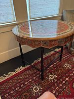 Round hand-painted side table with glass topper in natural light showing intricate design and metal base.