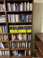 Full view of 6-shelf wooden bookcase filled with various books including a large series of yellow and black spine sports/golf instructional books and other varied titles
