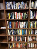 Full view of 6 shelf wooden bookcase filled with various books on multiple subjects.