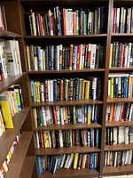 Front and side view of 6-shelf wooden bookcase filled mostly with hardcover books, some softcover, ranging across various subjects.