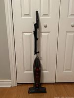 Full view of upright Dibea vacuum cleaner standing against white closet doors on floor.