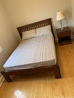 Full view of assembled double pine bedframe with mahogany stain showing headboard, footboard, and mattress with pillows in room with wood floor and nightstand.