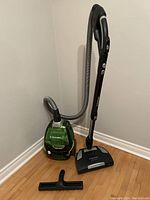 Full view of the vacuum with hose, main body, Deepclean head attachment, and flat brush attachment on wood floor.