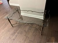 Photo showing the full glass top coffee table with brass-colored metal base on a wood floor. Glass top has scalloped edges. Metal base has decorative curved supports and four legs.