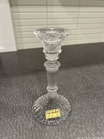 Clear vintage crystal candle holder with detailed cut and etched design, labeled Inn Crystal, displayed on a textured dark surface with blinds background.