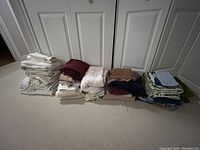 Photo showing multiple stacks of various bathroom towels including face cloths, floor towels, drying towels in various colors and conditions.