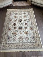Full view of rectangular wool area rug on dark hardwood floor with traditional floral and geometric patterns in light beige and multicolor.