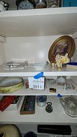 Three shelves containing assorted vintage decorative items including crystal sugar dish, ashtray, miniature porcelain items, elephant figurines, small picture frame, and vintage marbles.