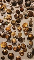 Photo showing a large assortment of gold and silver brass and concho sewing buttons spread out, various sizes and shapes visible