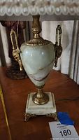 Close-up of marble urn-shaped lamp body with gold gilt handles and trim on a square marble footed base