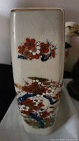 Close up of one side of the vase showing detailed plum blossom flowers in red, white, and gold with blue branches on crackled white ceramic.