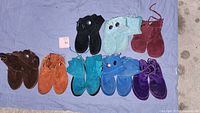 Overview of ten pairs of moccasins in various colors including brown, tan, black, teal, blue, purple, and burgundy, laid out on a blue cloth.