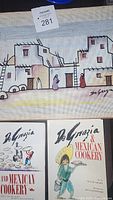 Two books with cover art by Ted De Grazia and titles referencing Mexican cookery by Rita Davenport, shown resting on top of an unfinished needlepoint artwork.