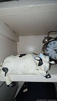 White sleeping cow figurine on shelf with alarm clock partially visible behind