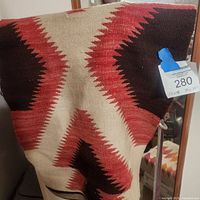 White blanket with red, brown geometric zigzag pattern draped on stand, showing design and texture.