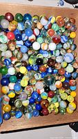 Top view of a wooden box filled with assorted vintage marbles showing a variety of colors and styles.