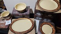 Photo showing oval plates, round dinner plates, bowls, and 16 oz mugs in original boxed packaging with Western belt pattern.