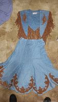 Denim skirt and wrap top with brown Western trim and fringe laid flat on carpeted floor, showing front details of skirt and top.