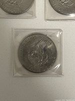 Three Eisenhower dollar coins touching each other, each in square clear plastic protective covers showing reverse side with eagle.