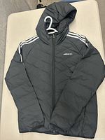 Front view of black Adidas Neo jacket showing quilted pattern, hood, and white stripe shoulder details with logo on chest.