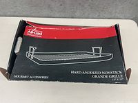Closed box showing All-Clad branding and illustration of the grill pan with handles. Described as hard-anodized nonstick grande grille, 13" x 20".