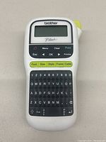 Front view of the Brother P-Touch handheld label printer showing buttons, keyboard, and display screen.