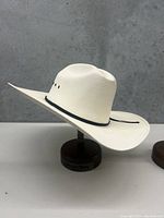 White cowboy hat shown on a wooden stand against a gray background.