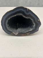 Front view of black geode showing hollow crystal-filled center and layered edges.