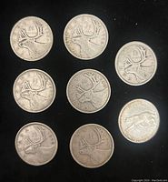 Seven Canadian silver 25 cent coins with caribou design and one coin with a bear design, arranged on a dark background.