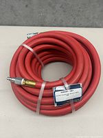 Coiled bright red flexible heat resistant hose with metal fittings on both ends and a label showing specifications.